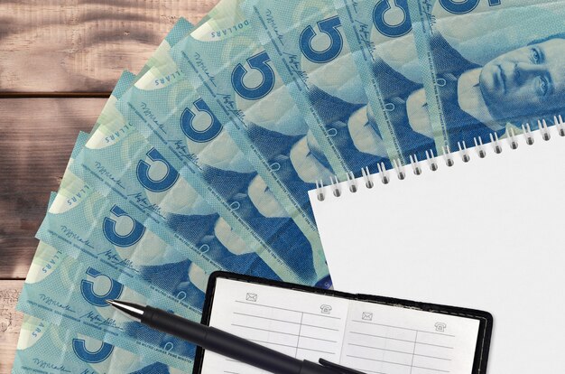 Abanico de billetes de dólares canadienses y bloc de notas con libro de contactos y bolígrafo negro
