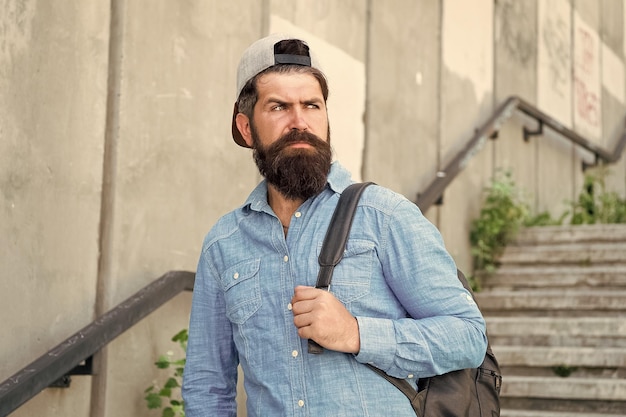 Abasteça sua alma com viagens homem confiante andar na rua cuidado de barbeiro masculino hipster brutal com mochila de viagem caminhadas conceito de aventura estilo urbano hipster maduro com viajante de barba homem barbudo