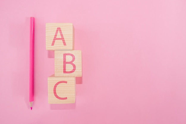 ABC letras del alfabeto en bloques cúbicos de madera en forma de pilar con un lápiz rosa sobre un fondo rosa. Copie el espacio. Concepto de escuela.