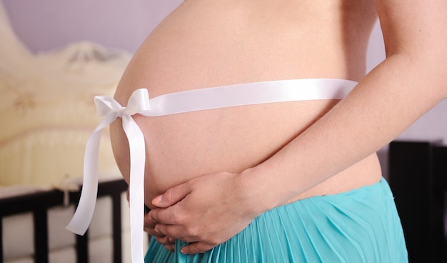 Abdomen de mujer embarazada con lazo blanco.