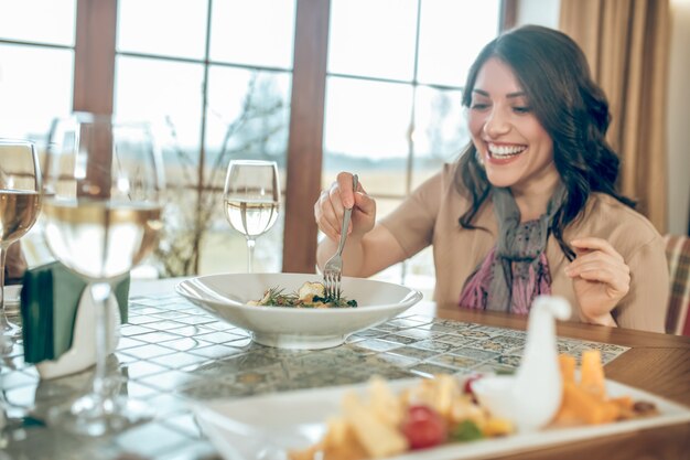 Abendessen. Dunkelhaarige süße Frau, die in einem Restaurant am Tisch sitzt und glücklich aussieht looking