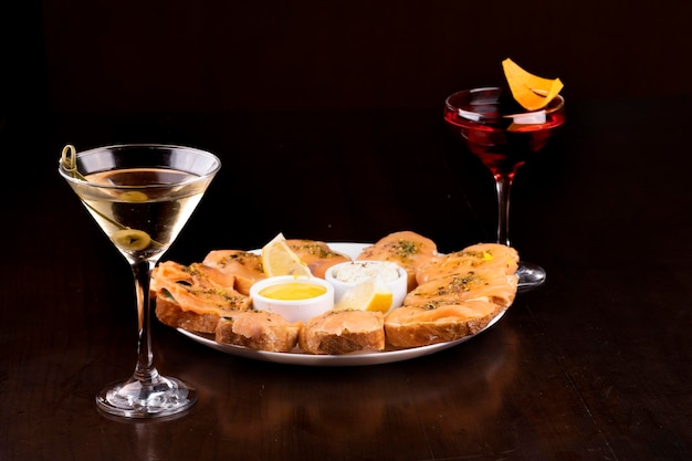 Abendessen mit Räucherlachs-Bruschetta mit Gurke und Mozzarella-Käse, zwei Gläser romantische Cocktails