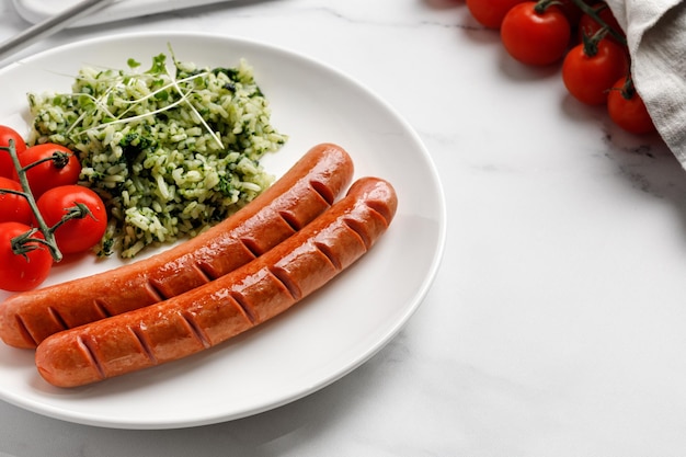 Abendgericht mit zwei gebratenen Würstchen und grünem Reis mit Spinat-Mikrogemüse und Kirschtomaten