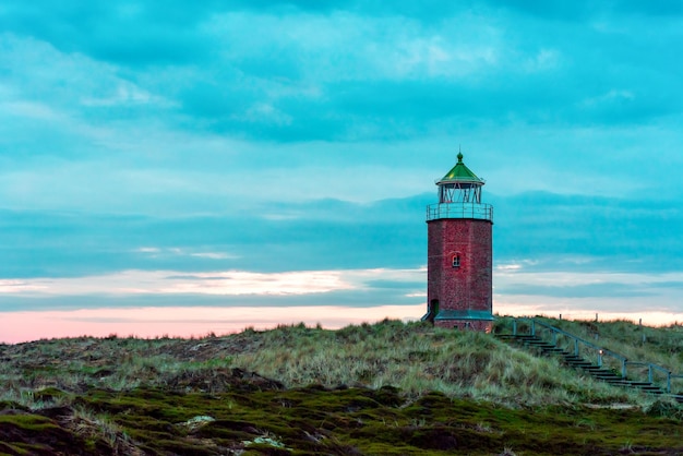 Abendlandschaft auf der Insel Sylt mit Marramgras, Hügeln, roten Ziegelsteinen, Leuchtturm und bewölkter Himmel Schöne Landschaft auf der deutschen Insel Sylt in der Nordsee