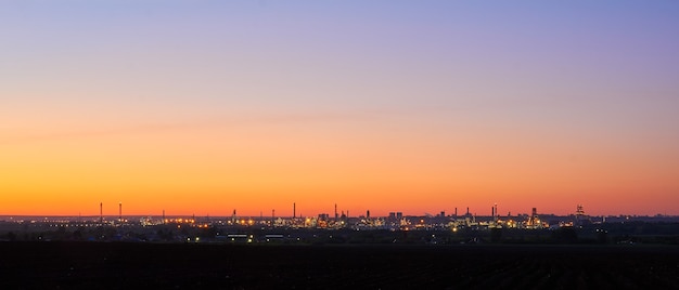 Abendliche Industrielandschaftssilhouette einer Ölraffinerie mit beleuchteten Lichtern am Horizont