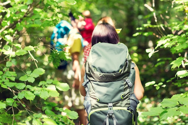 Abenteuer-, Reise-, Tourismus-, Wander- und Menschenkonzept - Nahaufnahme von Freunden, die mit Rucksäcken im Wald von hinten spazieren gehen