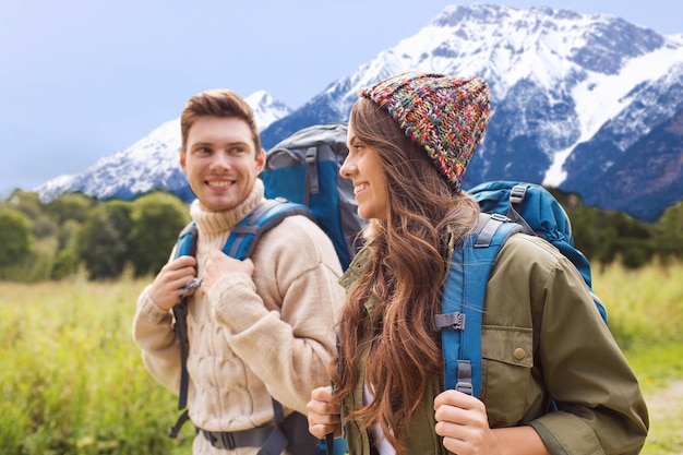 Abenteuer-, Reise-, Tourismus-, Wander- und Personenkonzept - lächelndes Paar, das mit Rucksäcken über den Berghintergrund geht