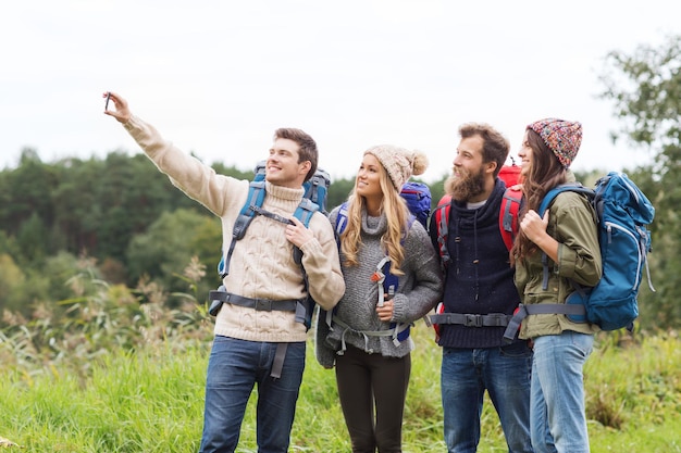 abenteuer, reise, tourismus, wanderung und personenkonzept - gruppe lächelnder freunde mit rucksäcken, die selfie machen
