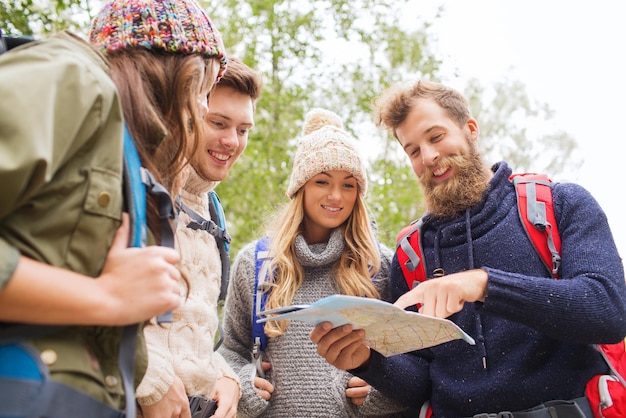 abenteuer, reise, tourismus, wanderung und personenkonzept - gruppe lächelnder freunde mit rucksäcken und karte im freien