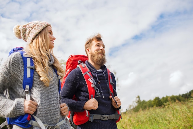 abenteuer, reise, tourismus, wanderung und personenkonzept - lächelndes paar, das mit rucksäcken im freien geht