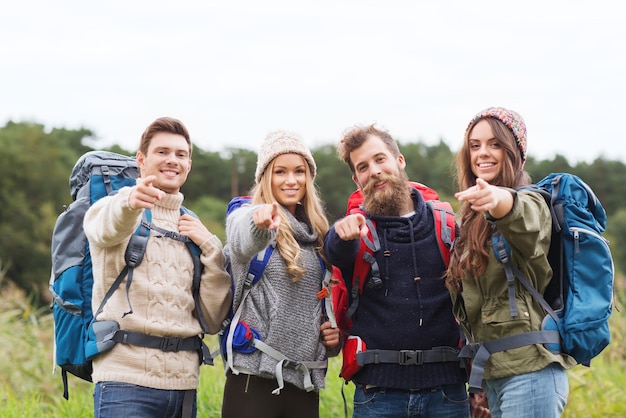 Abenteuer-, Reise-, Tourismus-, Wanderungs- und Personenkonzept - Gruppe lächelnder Freunde mit Rucksäcken, die mit dem Finger im Freien zeigen