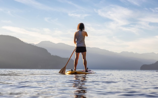 Abenteuerlustige Frau, die auf einem Paddelbrett in einem friedlichen See paddelt