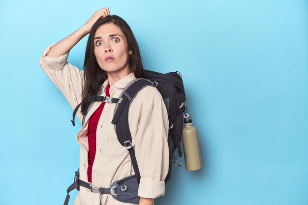 Abenteuerlustige Frau mit Rucksack auf Blau ist schockiert und erinnert sich an ein wichtiges Treffen