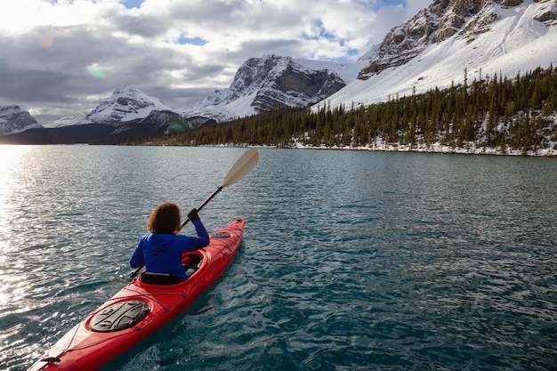 Abenteuerlustiges Mädchen beim Kajakfahren in einem Gletschersee, umgeben von den kanadischen Rocky Mountains