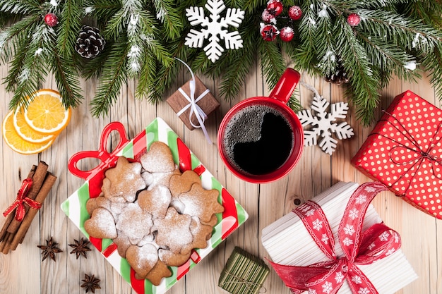 Abeto con adornos navideños, cajas de regalo, taza de café y dulces navideños sobre fondo de madera