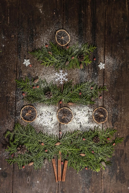 Abeto criativo de galhos verdes, fatias de limão secas e flocos de neve. Fundo de madeira, postura plana, decoração festiva, vista superior