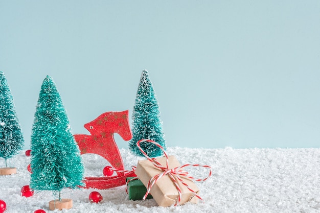 Abetos con juguete de caballo, cajas de regalo y frutos rojos sobre fondo de nieve