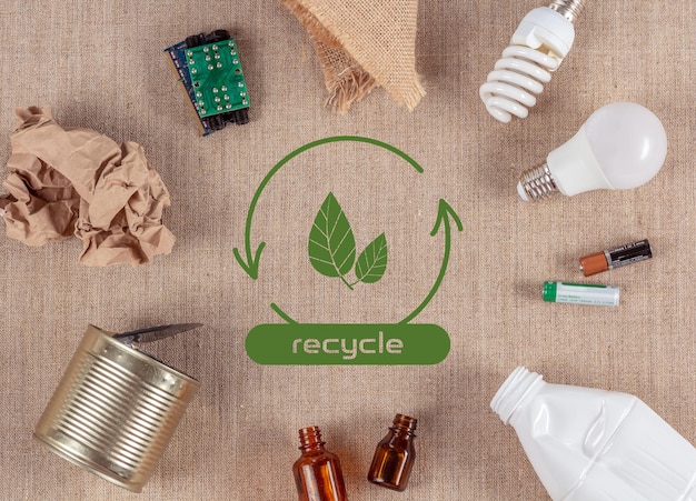Abfallsortierkonzept recycelbare Gegenstände auf Leinwandhintergrund mit grünen Blättern in der Mitte