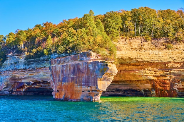 Abgebildete Felsen mit eisenroten und grünen Sommerbäumen auf Klippen mit Blick auf türkisgrünes Wasser