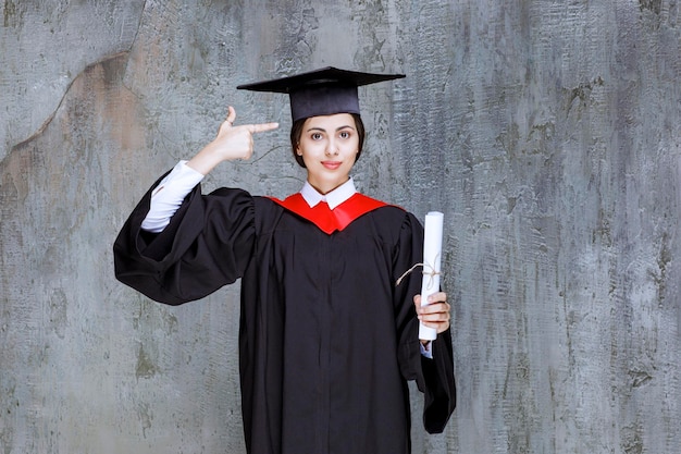 Abgeschlossene junge Frau im Kleid, das Universitätsdiplom hält. Foto in hoher Qualität