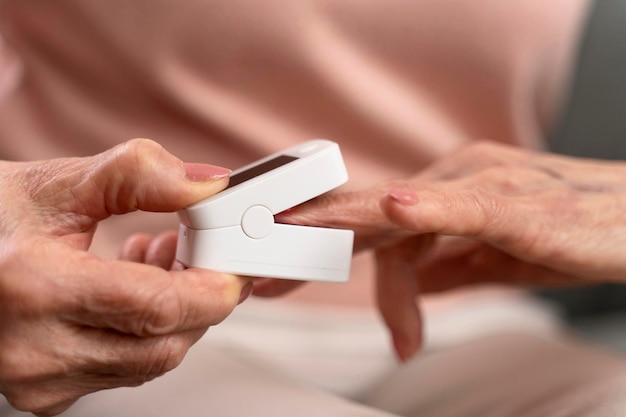 Abgeschnittene Ansicht der Seniorin mit Blutzuckertest am Finger im Wohnzimmer Gesundheitsinnovation und Alltag einer Diabetikerin mit Glukometer zur Überprüfung des Glukosespiegels in ihrem Haus