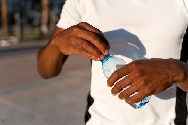 Abgeschnittene Ansicht des Afroamerikaners, der eine Plastikflasche mit Wasser hält