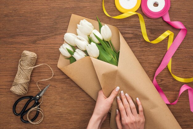 Abgeschnittene Ansicht eines Floristen, der Tulpenstrauß mit Schneidhandwerk auf Holzhintergrund herstellt