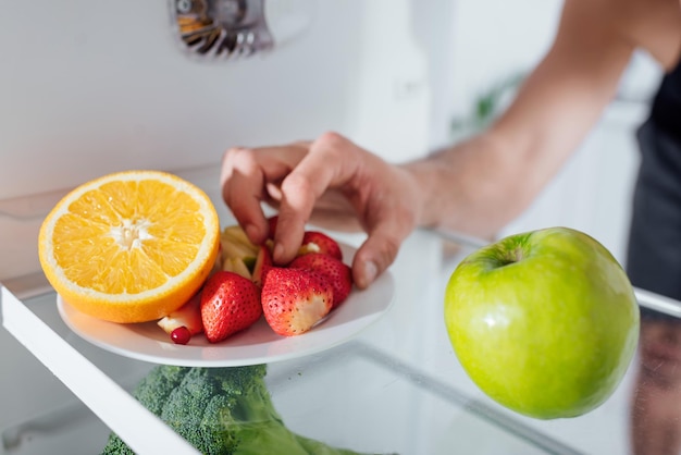 Abgeschnittene Ansicht eines Mannes, der Erdbeeren vom Teller im Kühlschrank nimmt