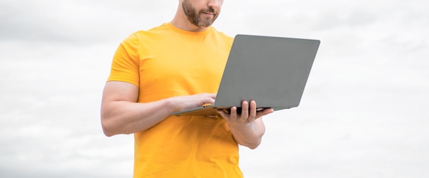 Abgeschnittene Ansicht eines Mannes, der online am Laptop auf Himmelshintergrund arbeitet