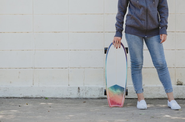 Abgeschnittene Aufnahme einer Frau in lässigem Outfit mit Surfskate gegen Betonwand. aktives Lifestyle-Konzept