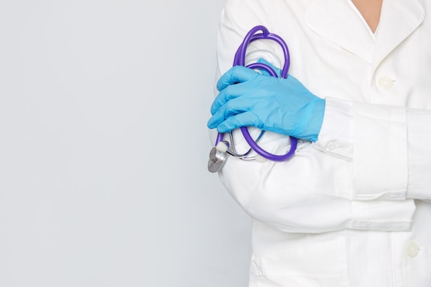 Abgeschnittene Aufnahme einer jungen Ärztin, die ein Stethoskop mit einem blauen medizinischen Handschuh in der Hand hält