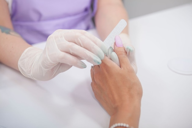 Abgeschnittene Aufnahme einer Maniküre, die den Daumenfingernagel einer Kundin feilt