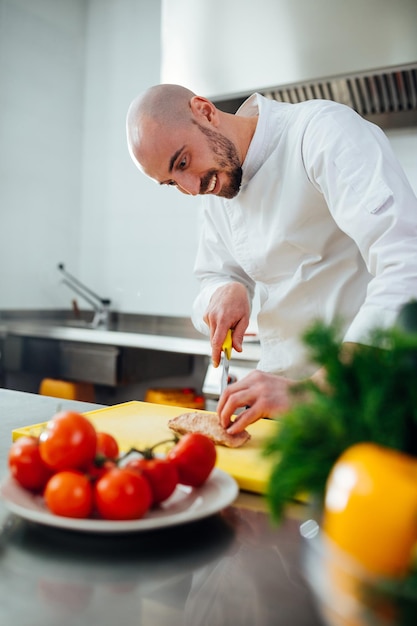 Abgeschnittene Aufnahme eines jungen männlichen Kochs, der das Fleisch in einer professionellen Küche schneidet