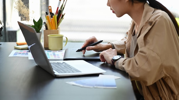 Abgeschnittene Aufnahme kreative Frau, die mit Laptop-Computer und Grafiktablett im Büro arbeitet