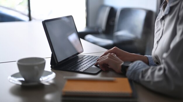 Abgeschnittene Hände der Geschäftsfrau, die auf der drahtlosen Tastatur eines digitalen Tablets am Schreibtisch tippen.