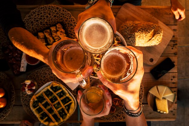 Abgeschnittene Hände einer Familie, die Biergläser über dem Tisch toastet