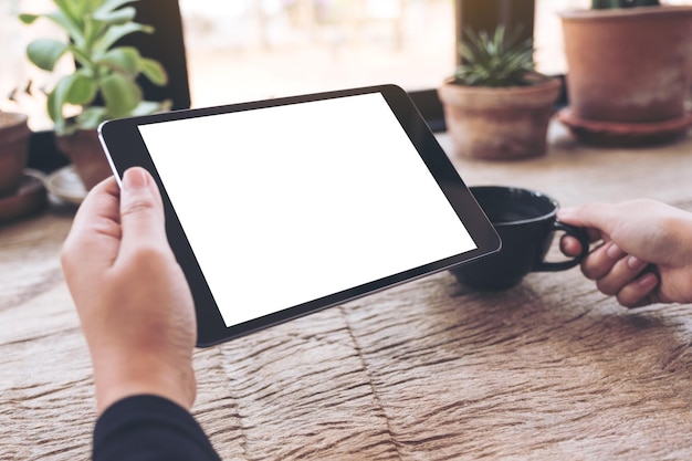 Abgeschnittene Hände einer Frau, die ein digitales Tablet mit Kaffee auf dem Tisch im Café benutzt