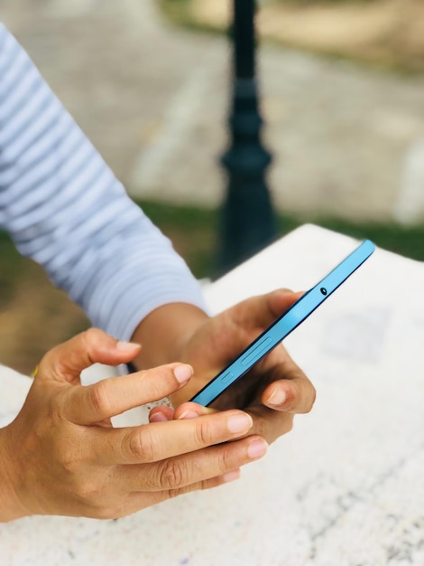 Abgeschnittene Hände einer Frau, die ein Handy auf dem Tisch benutzt