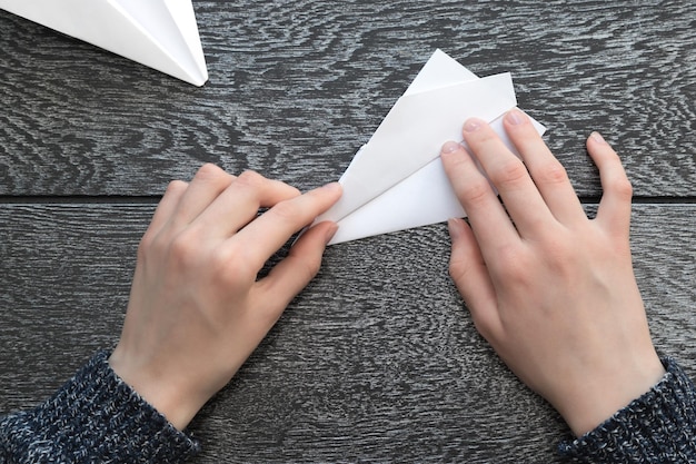 Foto abgeschnittene hände einer frau, die ein papierflugzeug auf einem holztisch herstellt