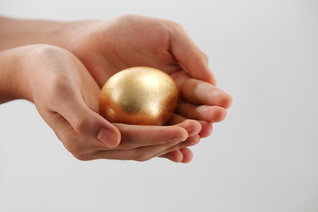 Abgeschnittene Hände einer Frau mit einem goldenen Ei auf einem grauen Hintergrund