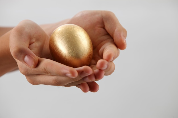 Abgeschnittene Hände einer Frau mit einem goldenen Ei auf einem grauen Hintergrund