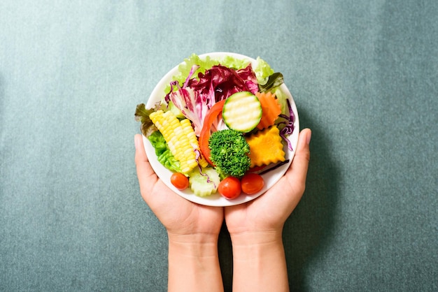 Abgeschnittene Hände einer Person, die Salat auf dem Tisch hält