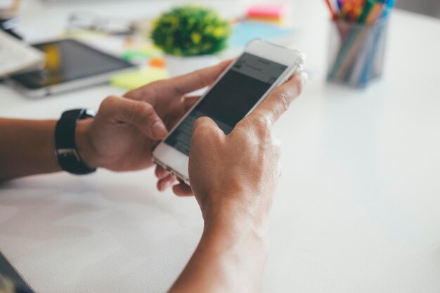 Foto abgeschnittene hände eines geschäftsmannes, der ein smartphone am schreibtisch benutzt