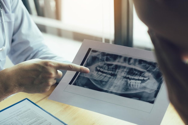 Abgeschnittene Hände eines männlichen Zahnarztes, der einem Patienten im Krankenhaus ein Röntgenbild erklärt
