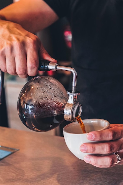 Abgeschnittene Hände eines Mannes, der im Café Kaffee in eine Tasse gießt