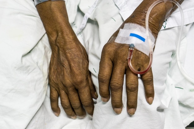Foto abgeschnittene hände eines patienten mit iv-tropfe im krankenhausbett