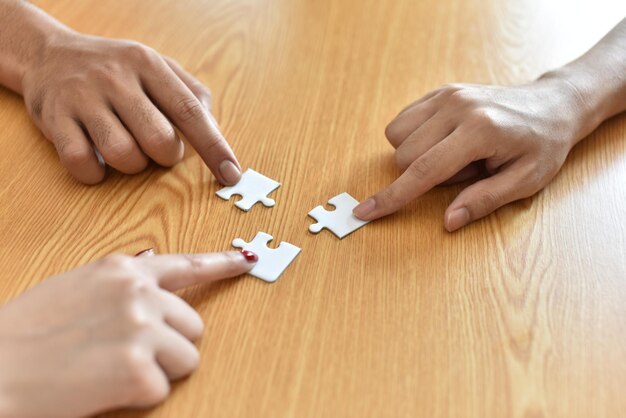 Foto abgeschnittene hände halten puzzle-stücke auf dem tisch