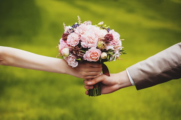 Foto abgeschnittene hände von braut und bräutigam, die einen blumenstrauß halten