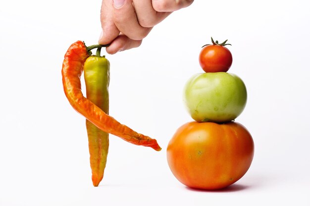 Foto abgeschnittene hand, die chili-pfeffer mit tomate auf weißem hintergrund hält