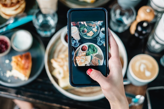 Abgeschnittene Hand einer Frau, die das auf dem Tisch servierte Essen fotografiert